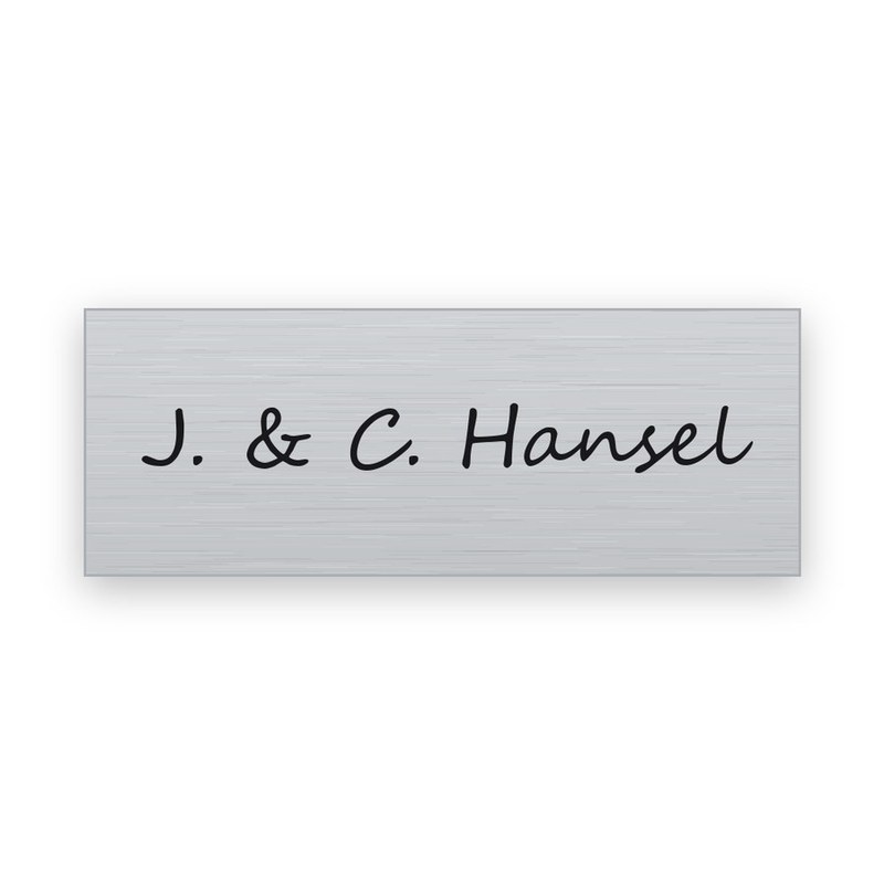 Rechteckiges silbernes Namensschild mit schwarzer Gravur in Schreibschrift, eine Zeile mit J. & C. Hansel
