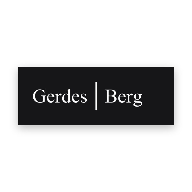 Rechteckiges schwarzes Türschild mit weißer Gravur, die Namen Gerdes und Berg nebeneinander, getrennt durch einen senkrechten Strich